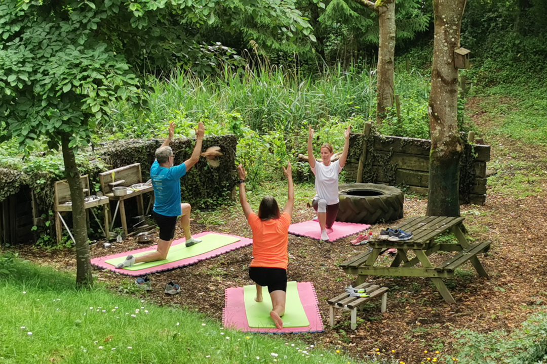 Two people doing pilates outside, being instructed by by a pilates teacher.